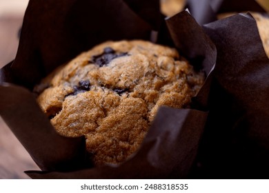 Freshly baked banana chocolate chip muffins wrapped in brown parchment paper, placed on a wooden cutting board alongside a bunch of ripe bananas. The rustic setup on a wooden table - Powered by Shutterstock