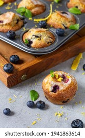 Freshly Baked Blueberry Muffin Cupcakes With Lemon Zest Mint In Metal Baking Tin And Wooden Tray On Grey Background 