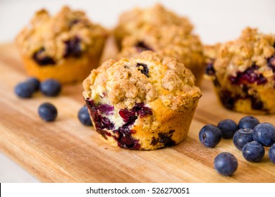 freshly baked blueberry muffins with an oat crumble topping on a natural wooden board