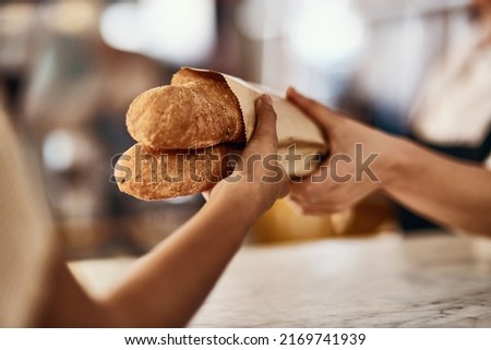 Freshly baked bread, one of lifes simplest pleasures. Cropped shot of a woman buying freshly made baguettes at a bakery.