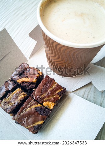 Freshly baked brownies with hot and cold latte in a takeaway cups.