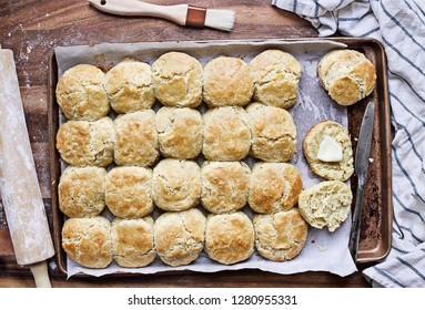 Freshly baked buttermilk southern biscuits or scones from scratch with rolling pin and basting brush on a baking sheet. Top view.