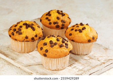 Freshly baked chocolate chip muffins on a wooden tray. Golden, fluffy muffins topped with melted chocolate chips, perfect for breakfast or dessert. Sweet, soft, and delicious bakery treat.