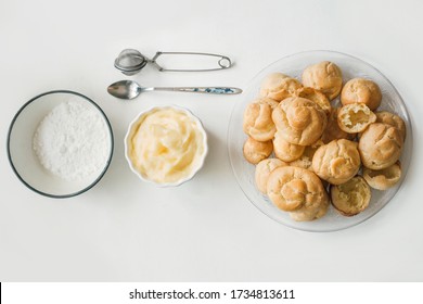 Freshly baked choux pastry dumplings, ready to be filled with vanilla custard and topped with icing sugar. French dessert recipe for cream puffs, profiteroles and eclairs. Culinary flat lay. Top view.