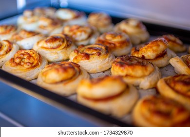 
Freshly baked, crispy, salty snails from puff pastry with ham and cheese in the oven. Fast food, quick and easy baking. Like pizza snails or pizza rolls.