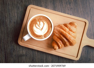 Freshly baked delicious croissant with cup of beautiful morning coffee on wooden cutting board, top view of breakfast table. 
