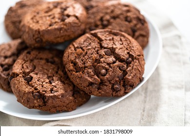 Freshly baked double chocolate chip cookies on a white plate.