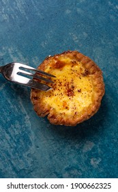 A Freshly Baked Egg Custard Tart Viewed From Above With A Cake Fork Resting On The Tart. The Tart Is On A Stone Blue Background