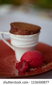 Freshly Baked And Fluffy Mini Chocolate Souffle Served In A Tiny Cup With Sweet And Tangy Raspberry Sorbet Ice Cream And Decorative Raspberry. Close Up.