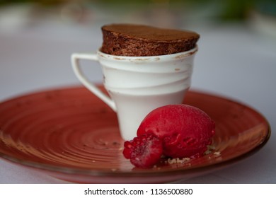 Freshly Baked And Fluffy Mini Chocolate Souffle Served In A Tiny Cup With Sweet And Tangy Raspberry Sorbet Ice Cream And Decorative Raspberry. Close Up.