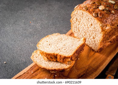 Freshly baked homemade organic multi-grain bread with pumpkin seeds on a cutting board on a black stone table. Copy space