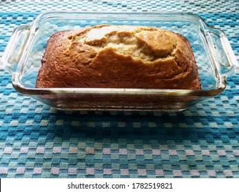 a freshly baked loaf of banana bread in a clear glass pyrex casserole dish resting on a blue towel