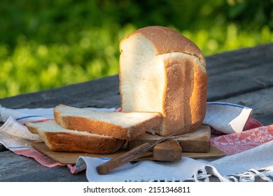A freshly baked loaf of white wheat bread on a wooden table in the garden. Thick slices of bread cut with a knife on a small tablecloth.