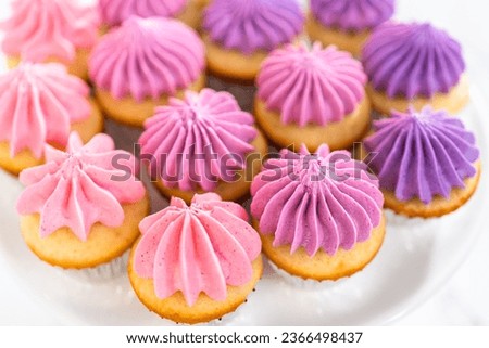 Freshly baked mini vanilla cupcakes with ombre pink buttercream frosting on a white cake stand.