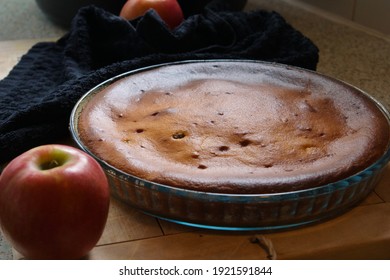 Freshly Baked Moist Quark Raisin Apple Cake In A Glass Mould On A Wooden Board With Apples On A Black Tea Towel