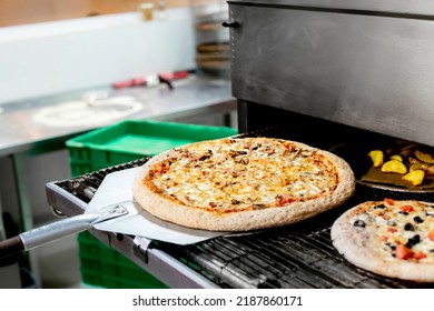 Freshly Baked Pizza With Cheese, Mushrooms, Ham On A Movable Pizza Oven Platform. The Working Area Of The Cafe Kitchen, Hot Shop, Pizza Oven, Food Industry.