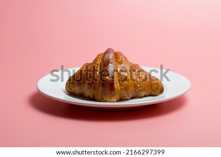 Freshly baked plain croissant on a plate against pink background.
