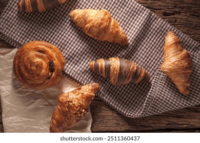 Freshly baked Raisin Danish Pastry and croissants. Arranged on a cloth and parchment paper. Top view and warm wooden background. - Powered by Shutterstock