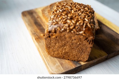 Freshly baked rectangular multigrain loaf placed on rustic wooden cutting board, crust coated with toasted sunflower seeds and whole grains, dense crumb