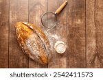 A freshly baked, rustic artisan bread loaf on a wooden table, accompanied by a dusting of flour and a metal sieve, evoking a sense of home baking and coziness.