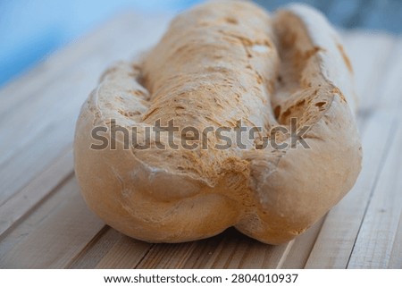 Freshly baked rustic bread loaf placed on a wooden table with a shallow depth of field. Traditional bakery product featuring a golden crust