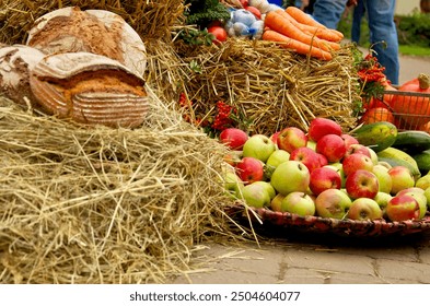 Freshly baked rustic bread, vibrant apples, and assorted vegetables are displayed on straw at a farmers’ market, creating a warm, inviting scene that highlights natural, locally sourced produce - Powered by Shutterstock