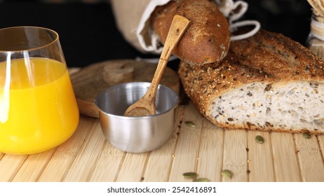 Freshly baked seeded bread in burlap sack, metal bowl with salt, wooden spoon, glass of orange juice on rustic wooden surface, creating wholesome, natural breakfast scene. - Powered by Shutterstock