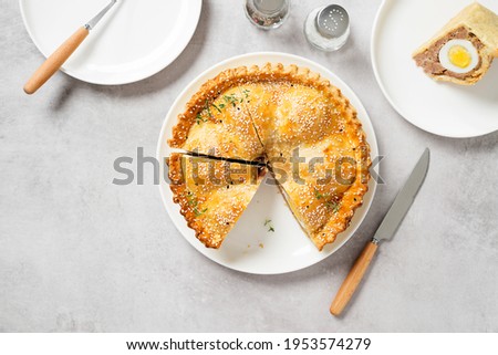Freshly baked a showstopping raised pie using sausagemeat and boiled eggs on light gray background, top view. Space for text