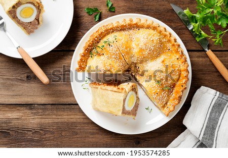 Freshly baked a showstopping raised pie using sausagemeat and boiled eggs on wooden background. top view