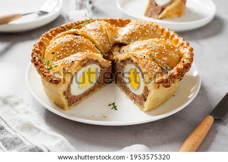 Freshly baked a showstopping raised pie using sausagemeat and boiled eggs on light gray background