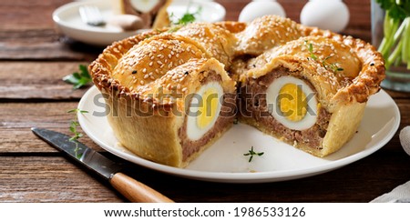Freshly baked a showstopping raised pie using sausagemeat and boiled eggs on wooden background. 