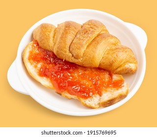 Freshly baked tasty croissant cut in half spreaded with red strawberry jam on white dish isolated on light orange background. Clipping path