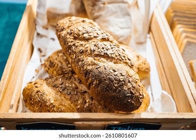 Freshly baked whole grain bread loaves covered with seeds displayed in a wooden basket at a bakery