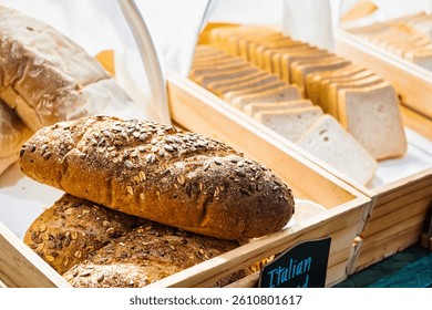 Freshly baked whole grain bread loaves covered with seeds displayed in a wooden basket at a bakery