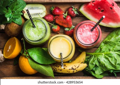 Freshly Blended Fruit Smoothies Of Various Colors And Tastes In Glass Jars In Rustic Wooden Tray. Yellow, Red, Green. Top View, Selective Focus