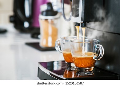 freshly brewed coffee is poured from the coffee machine into glass cups in the kitchen at home
