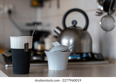 Freshly brewed tea in a mug standing on the kitchen table. In the background a metal kettle for heating water on a gas stove. - Powered by Shutterstock