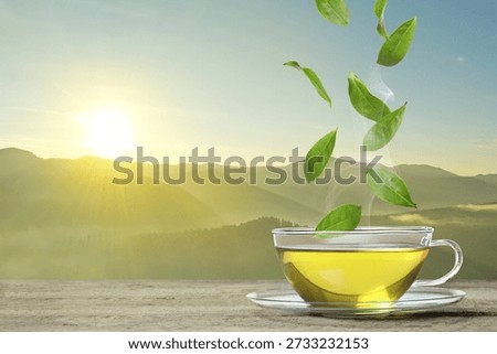 Freshly brewed tea on table in mountains. Green leaves flying above cup