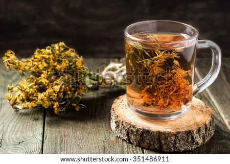 Freshly brewed tea with useful dried St. John's wort in a glass mug on a wooden table. Selective focus