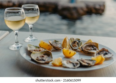 Freshly caught oysters on a plate and vine glasses. Restaurant on the shores of the Bay of Kotor near the oyster farm, Montenegro. Seafood. Beautuful seascape with oyster farm and mountains, Adriatic