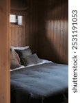 A freshly clean bedroom in a norwegian cabin for sale. A made king size bed for two. Pillows and sheets in earthy colors. A timber room with wood paneling. Professional photography for real estate.