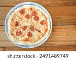 Freshly cooked Italian pizza with various cheese and sausage toppings in ceramic plate on wooden table. Empty blank copy text space.