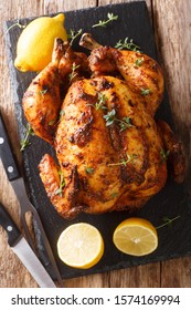Freshly cooked rotisserie chicken with ginger and spices close-up on a slate board on the table. Vertical top view from above