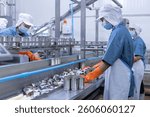 Freshly cut fish pieces move along a conveyor belt in a seafood processing plant, with empty cans and a worker wearing gloves.