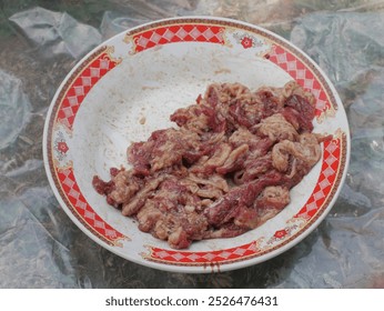 Freshly cut raw meat arranged on a traditional plate with red patterns. Ideal for barbecue preparation or traditional cooking methods. - Powered by Shutterstock