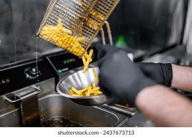 Freshly fried golden French fries being transferred from a metal basket to a stainless steel bowl in a commercial kitchen. - Powered by Shutterstock