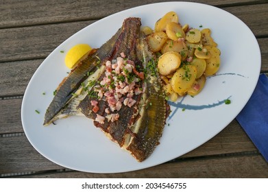 Freshly Fried Whole Plaice From The Baltic Sea With Bacon, Fried Potatoes And Chives Garnish On A Plate On A Wooden Table, High Angle View From Above