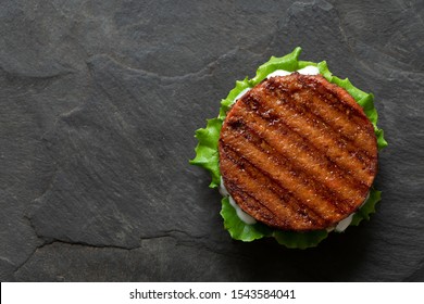 Freshly grilled plant based burger patty on bun with lettuce and sauce isolated on black slate. Top view. Copy space.