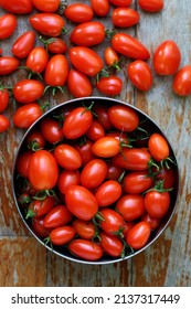 Freshly harvested cherry tomatoes. A metal bowl full of cherry tomatoes placed on a wooden textured bench. The vibrant red color is very eye-catching.