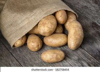 Freshly harvested organic russet baking potatoes spilling from a burlap bag onto a natural weathered wood table.  - Shutterstock ID 182758454